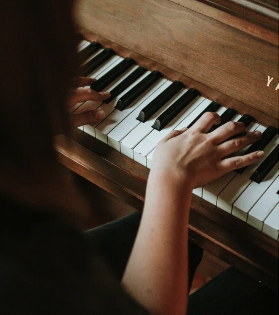Student's hands playing an upright piano